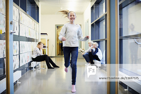 Smiling girl running in school corridor with friends in background