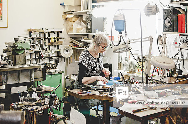 Senior female craftsperson working at workbench in jewelry workshop