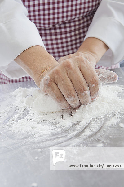 Hands of Hispanic woman kneading dough in flour