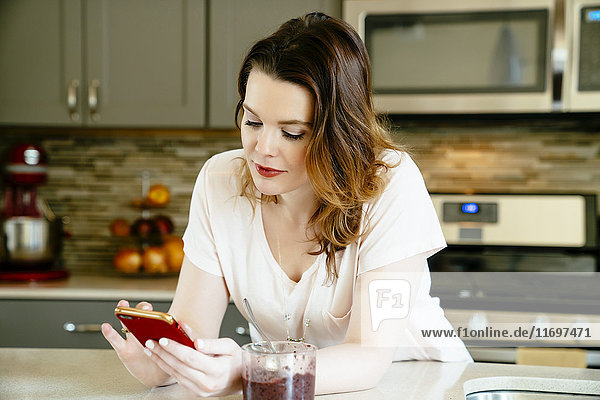 Frau  die in der heimischen Küche eine SMS auf ihrem Handy schreibt
