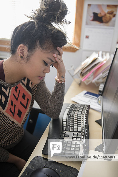 Frustrierte gemischtrassige Frau sitzt am Schreibtisch und benutzt einen Computer