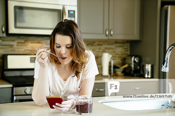Frau isst Smoothie und schreibt eine SMS mit ihrem Handy