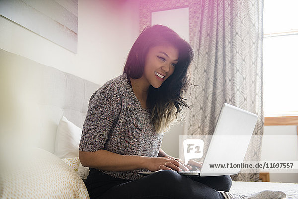 Gemischtrassige Frau sitzt auf dem Bett und benutzt einen Laptop