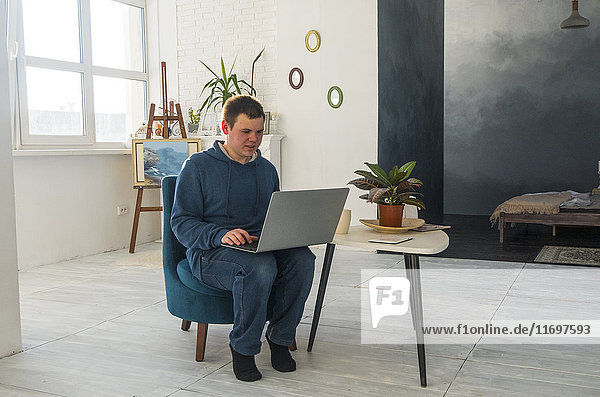 Kaukasischer Mann sitzt auf einem Stuhl und benutzt einen Laptop