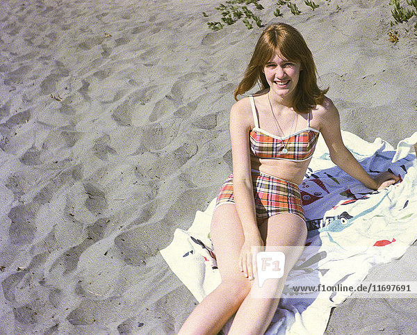 Portrait of smiling Caucasian teenage girl sitting on blanket at beach