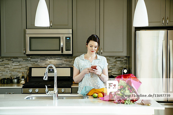 Frau  die in der heimischen Küche eine SMS auf ihrem Handy schreibt