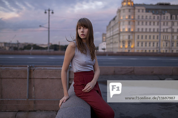Serious Caucasian woman sitting on wall in city