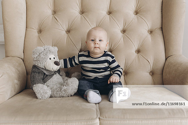 Portrait of Caucasian baby boy sitting on love seat with teddy bear