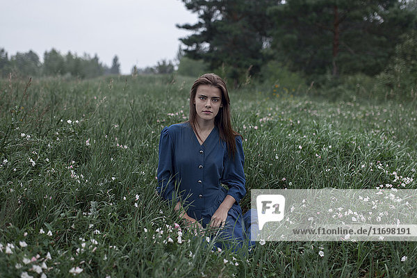 Serious Caucasian teenage girl sitting in field of wildflowers