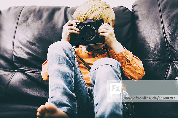 Kaukasischer Junge sitzt auf dem Sofa und benutzt die Kamera
