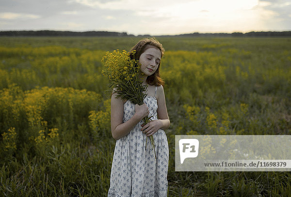 Kaukasisches Mädchen steht im Feld und hält einen Strauß Wildblumen