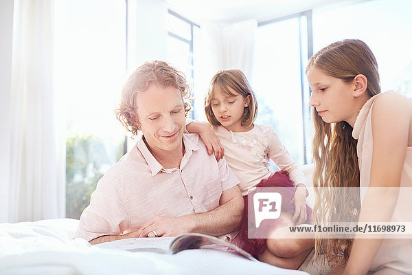 Father and daughters reading book on bed
