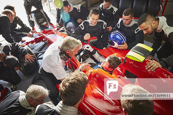 Manager and pit crew surrounding formula one driver in race car