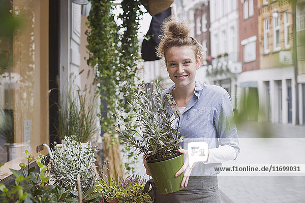 Porträt einer lächelnden Blumenhändlerin  die eine Topfpflanze im Schaufenster hält