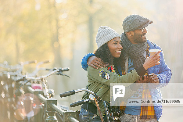 Junges Paar mit Fahrrad  das Kaffee trinkt und am Herbstgeländer entlang schaut  Amsterdam
