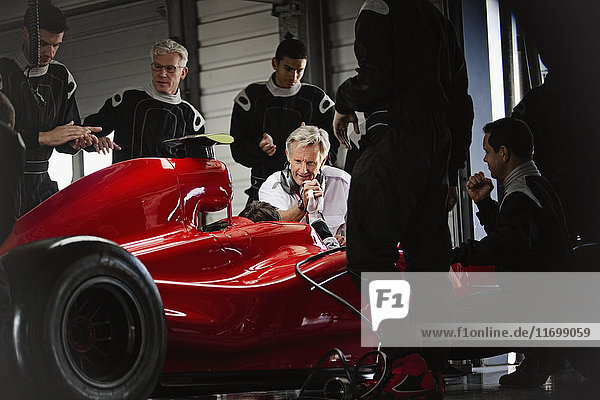 Manager and pit crew working on formula one race car in dark repair garage
