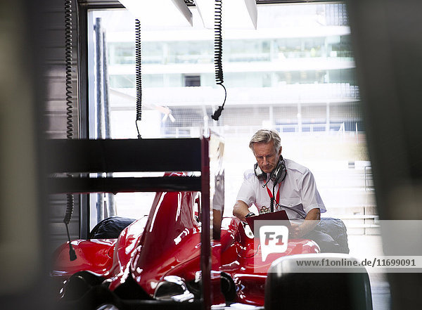 Manager with clipboard examining formula one race car in repair garage