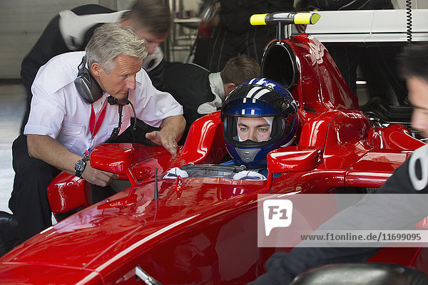 Manager talking to formula one race car driver in repair garage