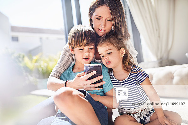 Mutter und Kinder mit dem Handy im sonnigen Wohnzimmer