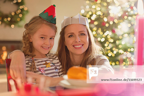 Porträt lächelnde Mutter und Tochter mit Elfenhut und Papierkrone am Weihnachtstisch