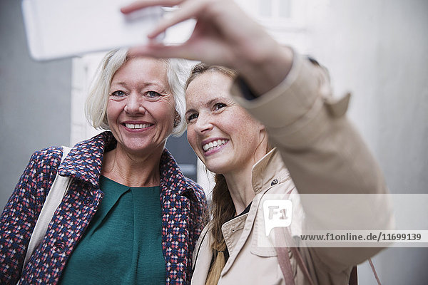 Smiling mother and daughter taking selfie with camera phone