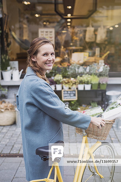 Portrait smiling woman walking bicycle at urban storefront