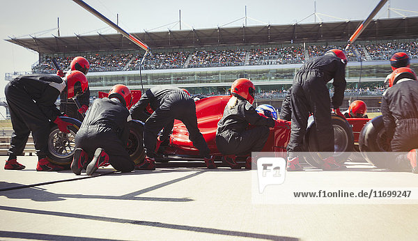 Pit crew replacing tires on formula one race car in pit lane