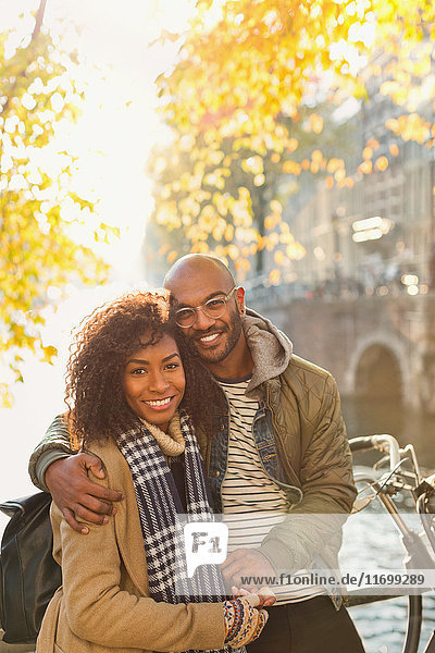 Portrait smiling  affectionate couple hugging along sunny autumn canal