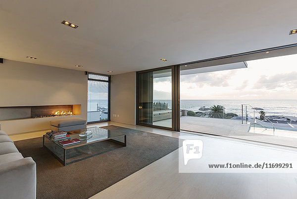 Modern  minimalist luxury living room with gas fireplace and patio doors open to ocean view and patio