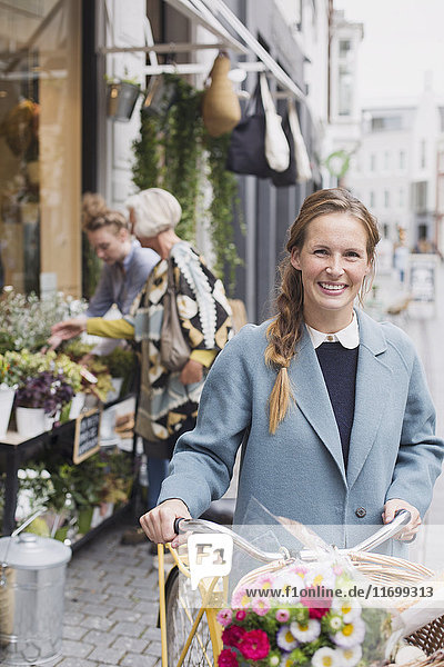 Porträt lächelnde Frau mit Fahrrad und Blumen im Korb vor einem Geschäft