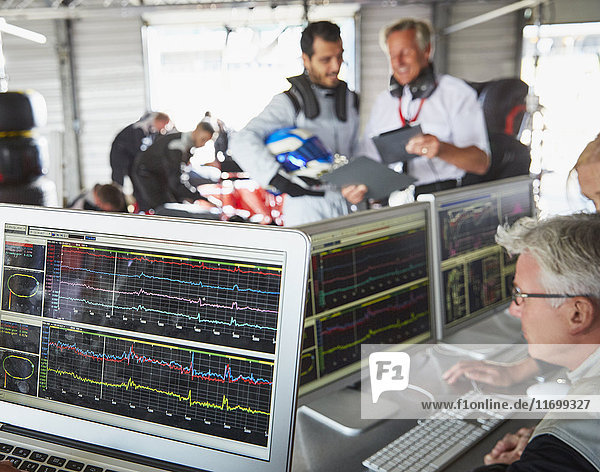 Formula one racing team reviewing diagnostics on computers in repair garage