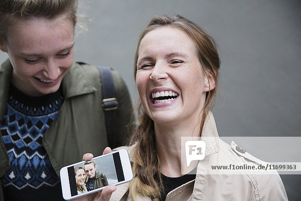 Laughing young women showing selfie photograph on smart phone