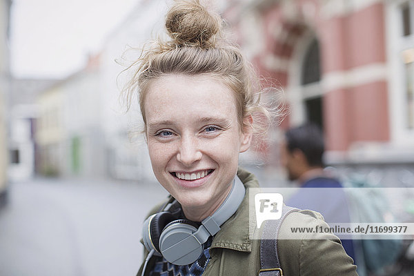 Porträt lächelnde junge Frau mit Kopfhörern auf der Straße in der Stadt
