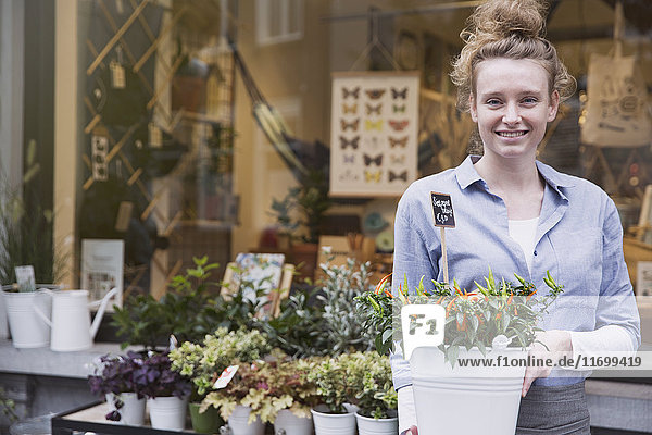 Porträt einer lächelnden Blumenhändlerin mit Topfpflanze im Schaufenster