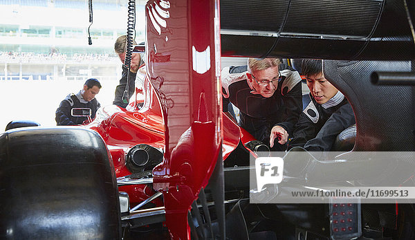 Pit crew mechanics examining race car in repair garage