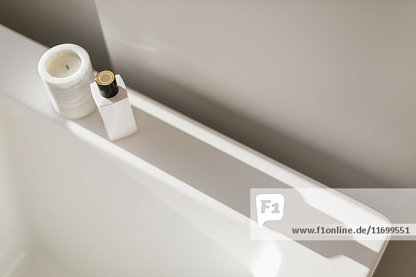 Candle and bottle casting shadow on ledge of white bathtub