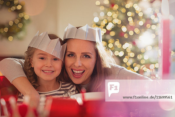 Porträt begeisterte Mutter und Tochter in Papierkronen am Weihnachtsessenstisch