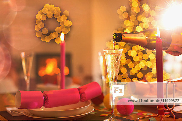 Pouring champagne into champagne flute on Christmas dinner table with Christmas cracker
