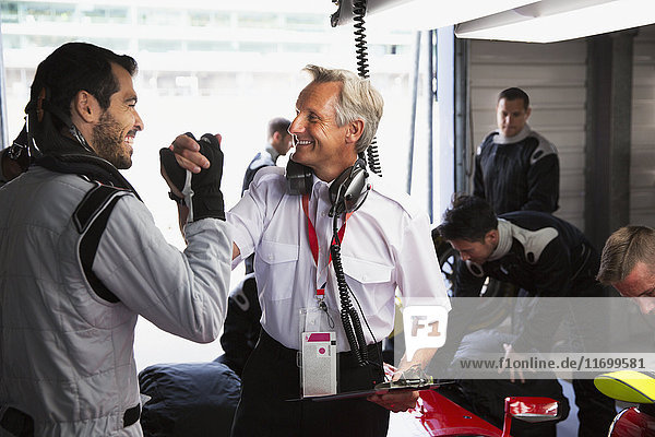 Manager and formula one driver celebrating  handshaking in repair garage