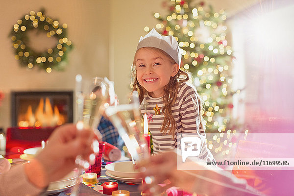 Portrait lächelndes Mädchen mit Papierkrone am Weihnachtstisch