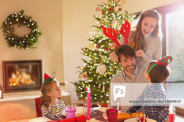 Familie mit Elfe und kostümiertem Rentiergeweih am weihnachtlichen Esstisch