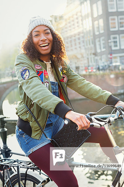 Portrait playful young woman bike riding along urban canal