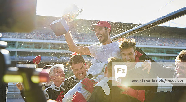 Formula one racing team carrying driver with trophy on shoulders  celebrating victory