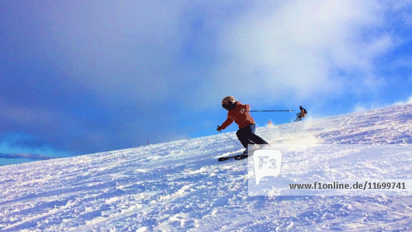 Skifahrer auf Skipiste mit wirbelndem Schnee zu Füßen
