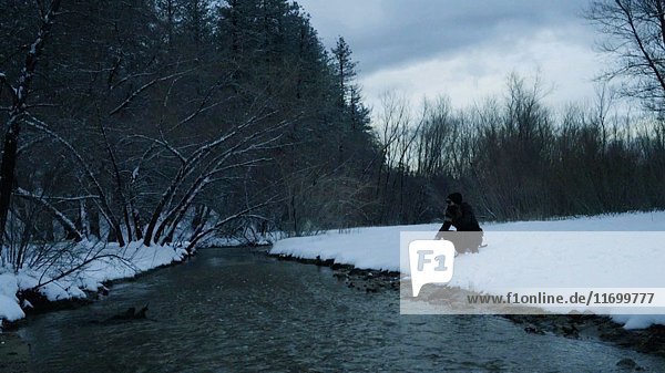 Man Crouching near Stream with Cloud Movement in Winter