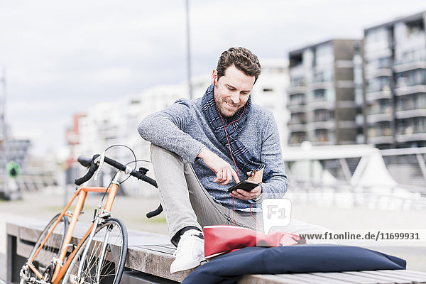 Geschäftsmann in der Stadt mit Fahrrad über Smartphone und Kopfhörer