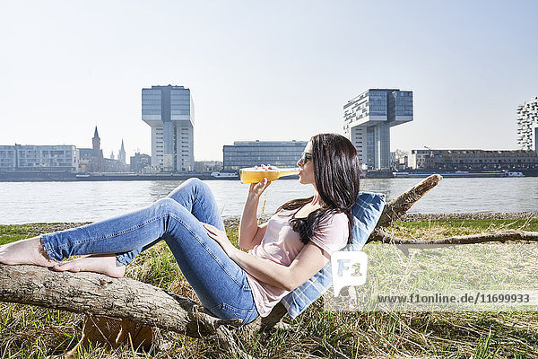 Germany  Cologne  young woman relaxing and having a beer at River Rhine