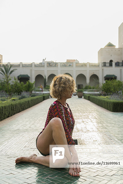 Marokko  Marrakesch  Tourist auf dem Boden sitzend in einem Innenhof beim Yoga