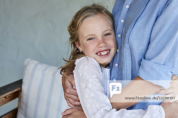 Porträt eines lächelnden kleinen Mädchens mit Zahnlücke  das seine Mutter umarmt.