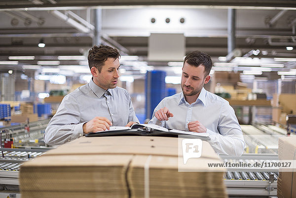 Two men in factory warehouse looking at documents